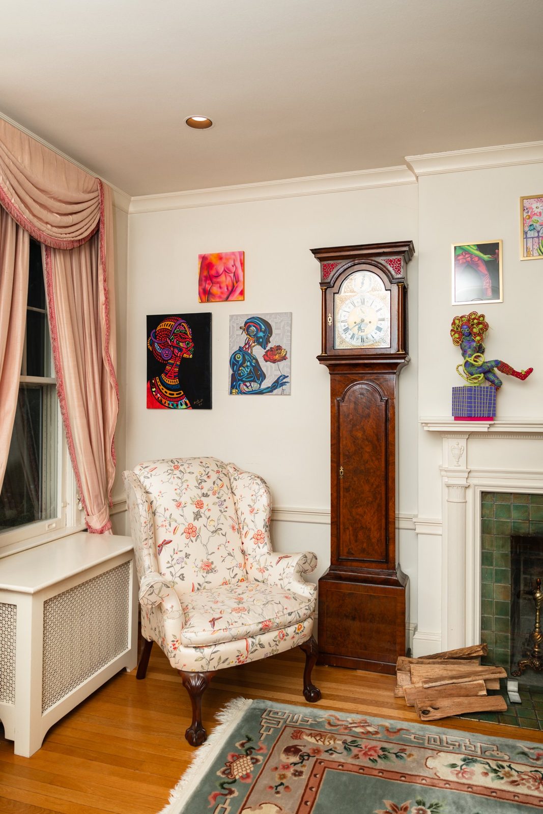 Paintings hung around a tall clock and a floral armchair at Girlism